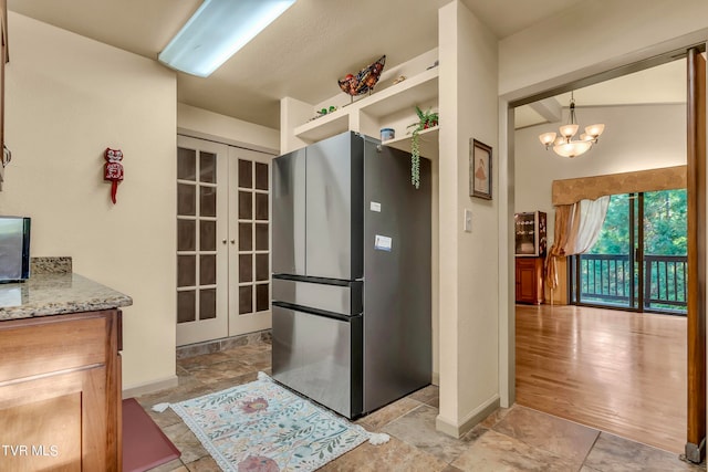 kitchen with light stone countertops, stainless steel fridge, french doors, a notable chandelier, and light hardwood / wood-style floors