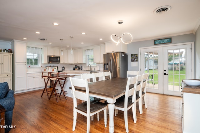 dining space featuring french doors, crown molding, light hardwood / wood-style floors, and a wealth of natural light