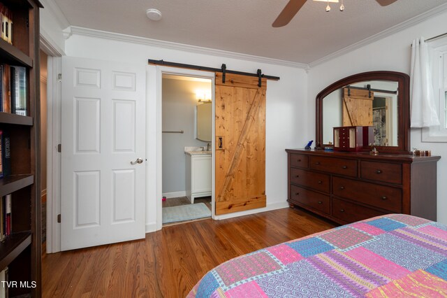 bedroom featuring ceiling fan, connected bathroom, ornamental molding, dark wood-type flooring, and a barn door