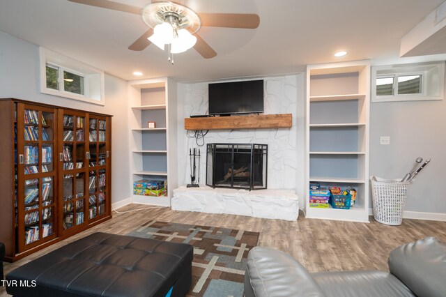 living room featuring wood-type flooring, a stone fireplace, and ceiling fan