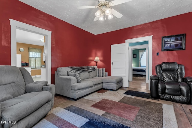 living room with ceiling fan, a textured ceiling, and light wood-type flooring