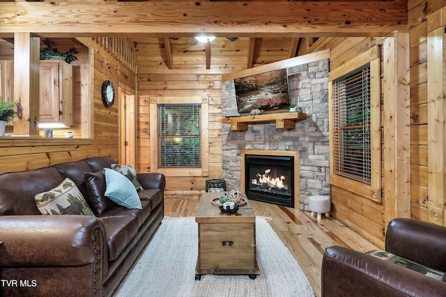 living room featuring light hardwood / wood-style floors, beam ceiling, wood walls, a fireplace, and ceiling fan