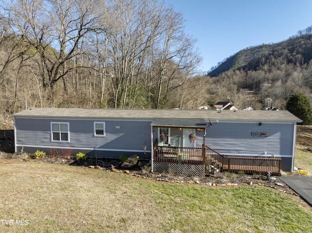 manufactured / mobile home featuring a front yard, a deck with mountain view, and a forest view