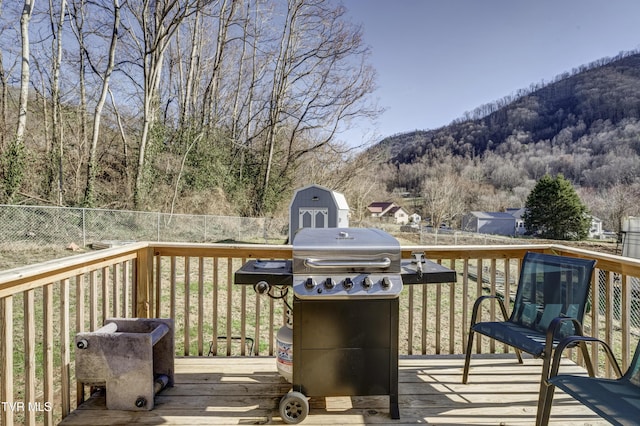 wooden terrace featuring a grill, fence, a wooded view, and a mountain view