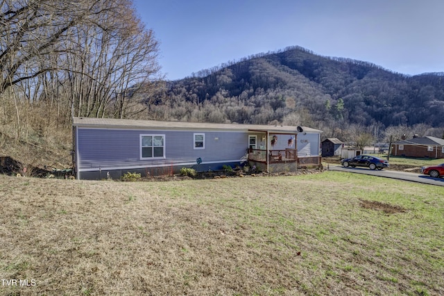 manufactured / mobile home with a deck with mountain view, a front lawn, and a wooded view