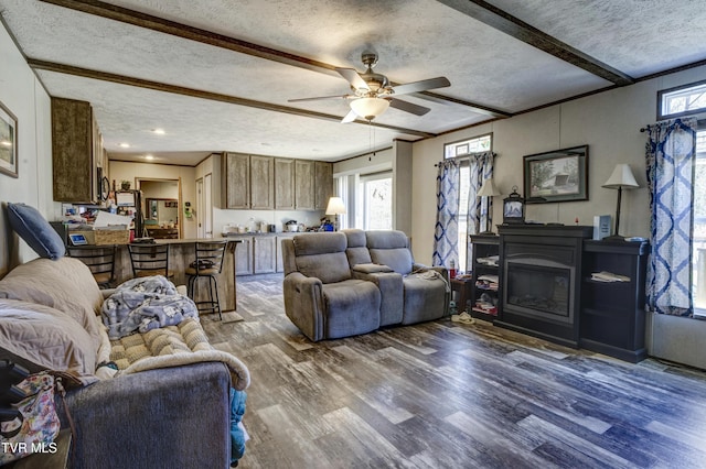 living area featuring a textured ceiling, wood finished floors, a ceiling fan, beam ceiling, and a glass covered fireplace