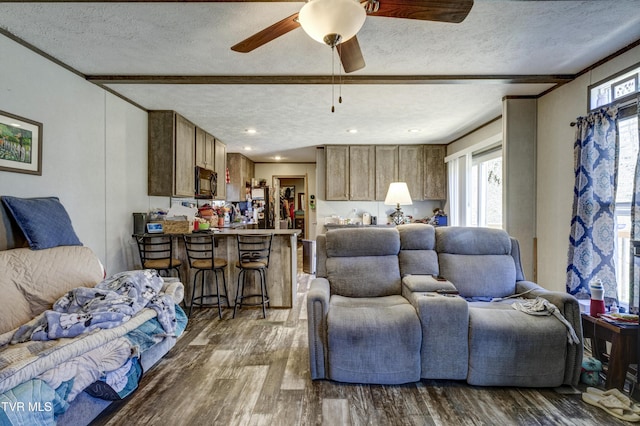 living area with ceiling fan, a textured ceiling, wood finished floors, and beamed ceiling