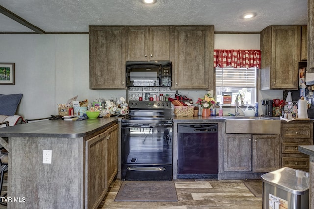 kitchen featuring a peninsula, wood finished floors, a sink, black appliances, and dark countertops