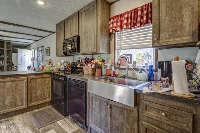 kitchen with dark countertops, a sink, a textured ceiling, wood finished floors, and black appliances