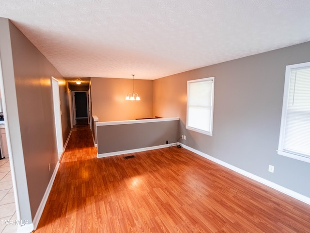 spare room featuring a notable chandelier, wood-type flooring, and a textured ceiling