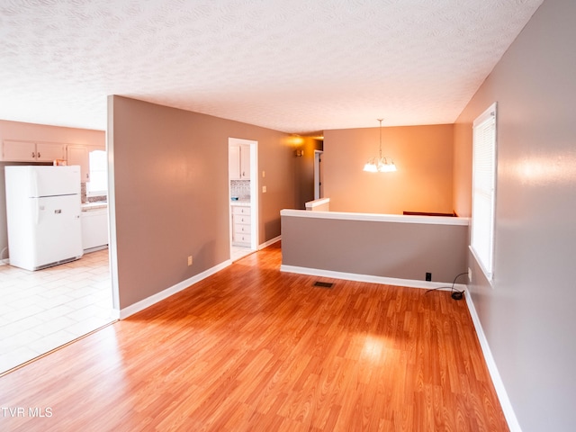 empty room featuring light hardwood / wood-style flooring, a chandelier, and a textured ceiling