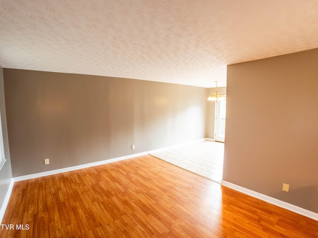 empty room featuring a notable chandelier, wood-type flooring, and a textured ceiling