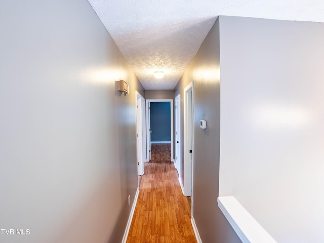 hallway with light hardwood / wood-style floors and a textured ceiling