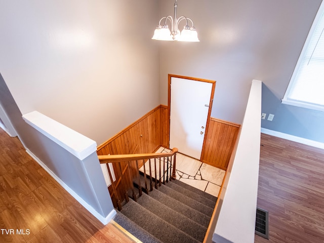 stairs featuring a notable chandelier, wooden walls, and hardwood / wood-style floors