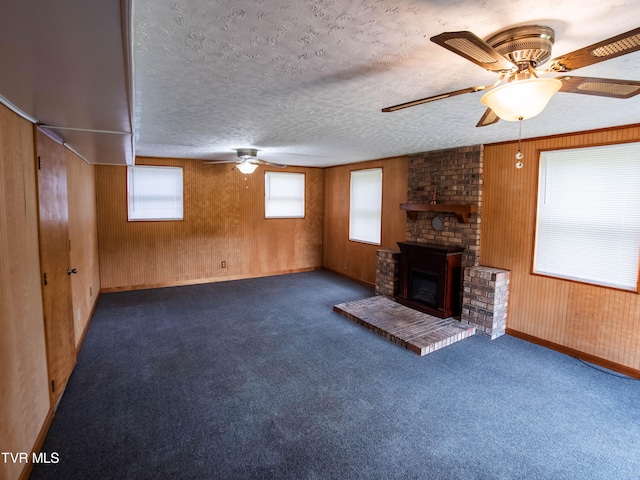 unfurnished living room with a fireplace, a textured ceiling, dark colored carpet, ceiling fan, and wooden walls