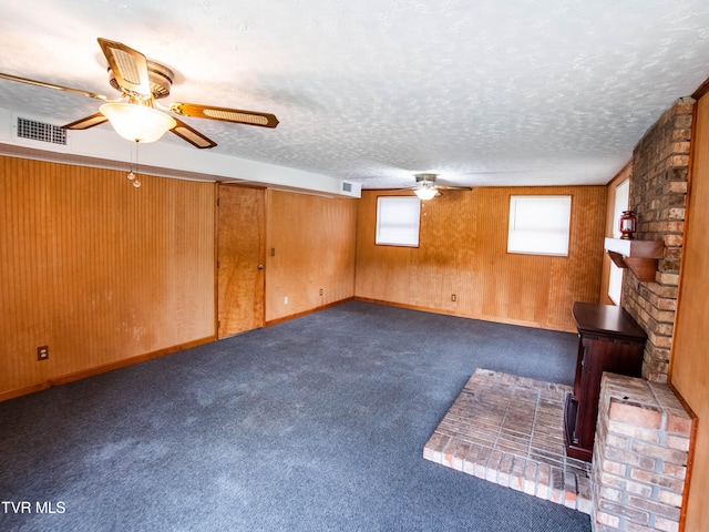 basement with a textured ceiling, wood walls, ceiling fan, and dark carpet