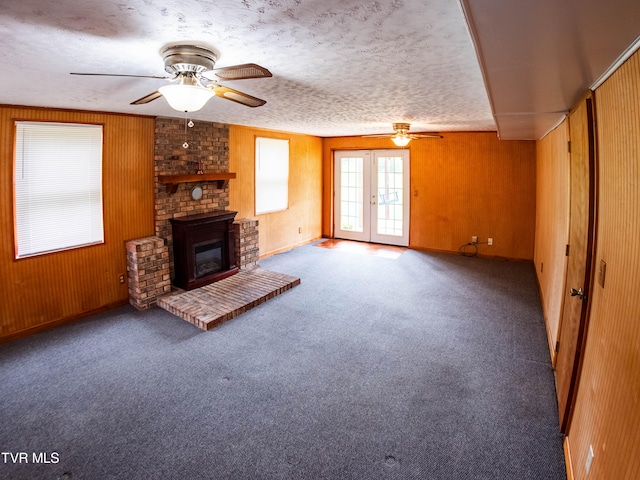 unfurnished living room featuring carpet flooring, wooden walls, ceiling fan, and a fireplace