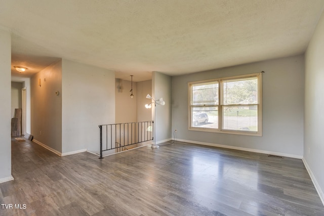 empty room featuring a chandelier, a textured ceiling, and dark hardwood / wood-style floors