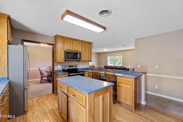 kitchen with a textured ceiling, stainless steel appliances, light wood-type flooring, and a kitchen island