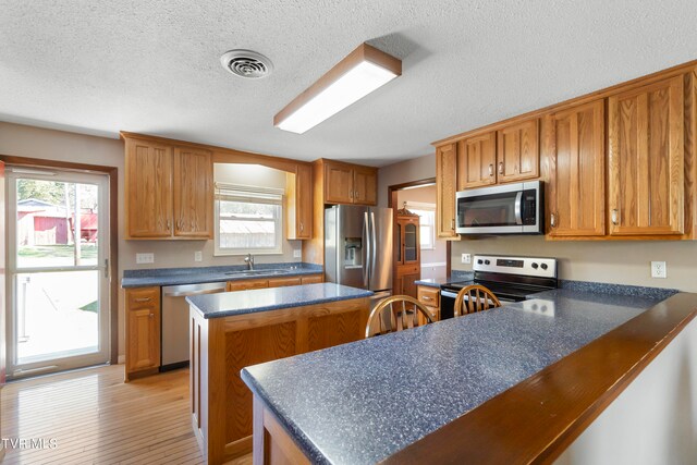 kitchen with sink, a kitchen island, a textured ceiling, appliances with stainless steel finishes, and light hardwood / wood-style floors