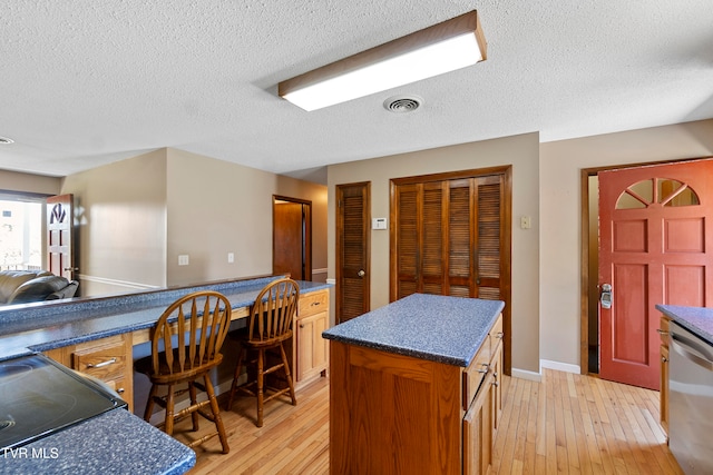 kitchen with a kitchen island, built in desk, stainless steel dishwasher, and light hardwood / wood-style flooring