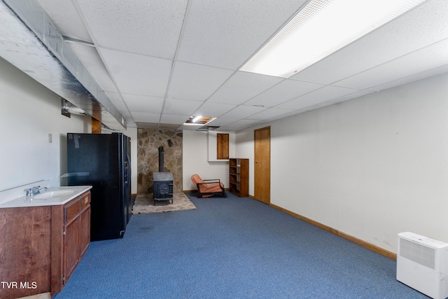 basement with carpet flooring, sink, a wood stove, a drop ceiling, and black refrigerator