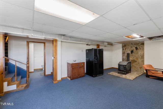 basement featuring black fridge, a drop ceiling, carpet, and a wood stove