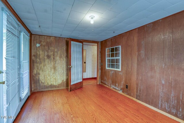 unfurnished bedroom with light wood-type flooring, wood walls, and multiple windows