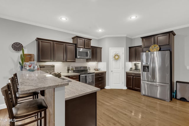 kitchen featuring light wood finished floors, backsplash, appliances with stainless steel finishes, dark brown cabinets, and a peninsula