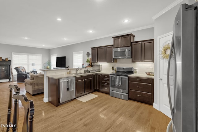 kitchen featuring stainless steel appliances, light wood-style flooring, open floor plan, a sink, and dark brown cabinetry