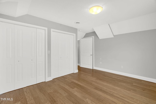 unfurnished bedroom featuring lofted ceiling, wood finished floors, two closets, and baseboards