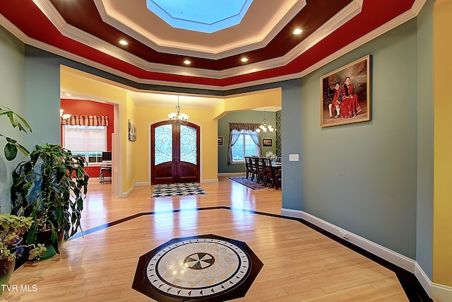 entrance foyer with a tray ceiling, light hardwood / wood-style flooring, an inviting chandelier, crown molding, and french doors