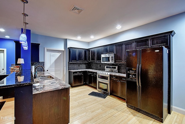 kitchen with dark stone countertops, light hardwood / wood-style floors, appliances with stainless steel finishes, and sink