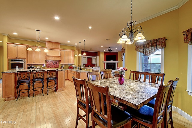 dining area featuring light wood-type flooring, ceiling fan with notable chandelier, crown molding, and sink