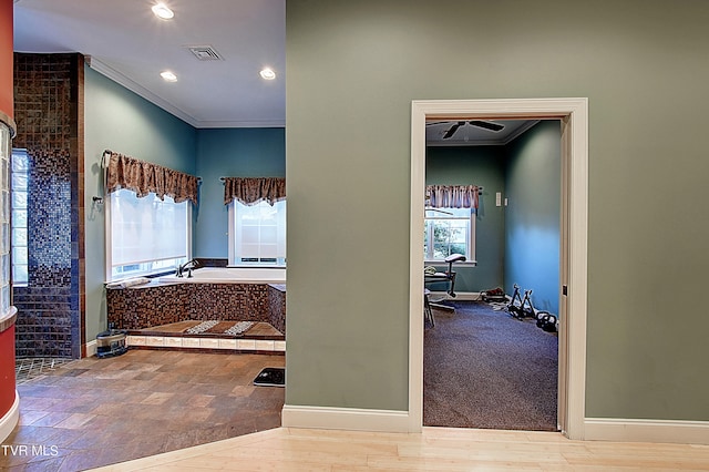 bathroom with a tub to relax in, crown molding, and a wealth of natural light