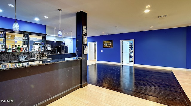 kitchen featuring light hardwood / wood-style flooring, dark stone counters, hanging light fixtures, and black fridge