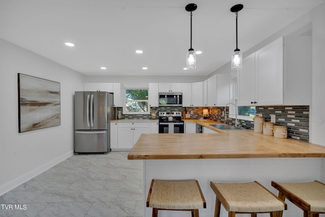 kitchen featuring kitchen peninsula, a kitchen bar, stainless steel appliances, sink, and white cabinetry