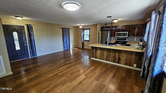 kitchen featuring tasteful backsplash, kitchen peninsula, stainless steel appliances, dark brown cabinets, and dark hardwood / wood-style floors