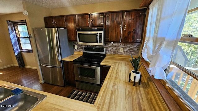 kitchen featuring stainless steel appliances, backsplash, a textured ceiling, and dark hardwood / wood-style floors