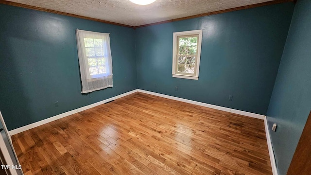 empty room with ornamental molding, wood-type flooring, and a textured ceiling