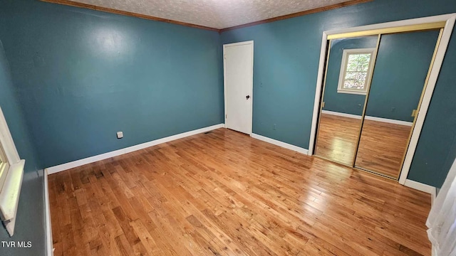 unfurnished bedroom with a textured ceiling, crown molding, hardwood / wood-style floors, and a closet