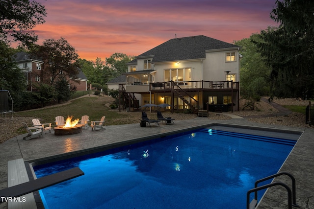 pool at dusk featuring a diving board, a fire pit, a patio area, and a deck