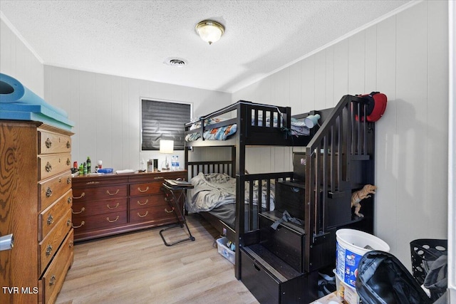 bedroom with wood walls, light hardwood / wood-style floors, ornamental molding, and a textured ceiling