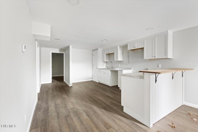 kitchen featuring sink, a kitchen breakfast bar, kitchen peninsula, wood-type flooring, and white cabinets