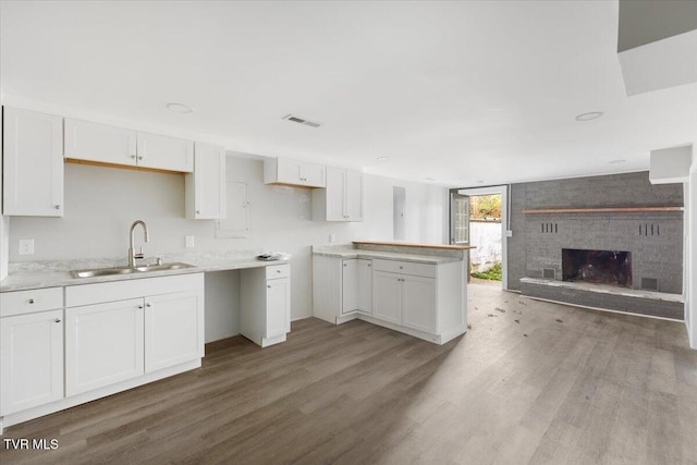 kitchen with hardwood / wood-style floors, white cabinetry, sink, and a brick fireplace