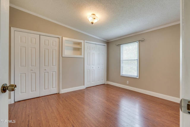 unfurnished bedroom with wood-type flooring, crown molding, multiple closets, vaulted ceiling, and a textured ceiling