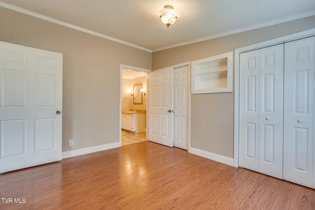 unfurnished bedroom featuring multiple closets, a textured ceiling, light hardwood / wood-style flooring, and ornamental molding