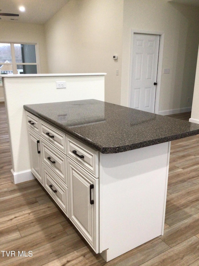 kitchen with ceiling fan, dark stone countertops, white cabinets, a center island, and dark hardwood / wood-style floors