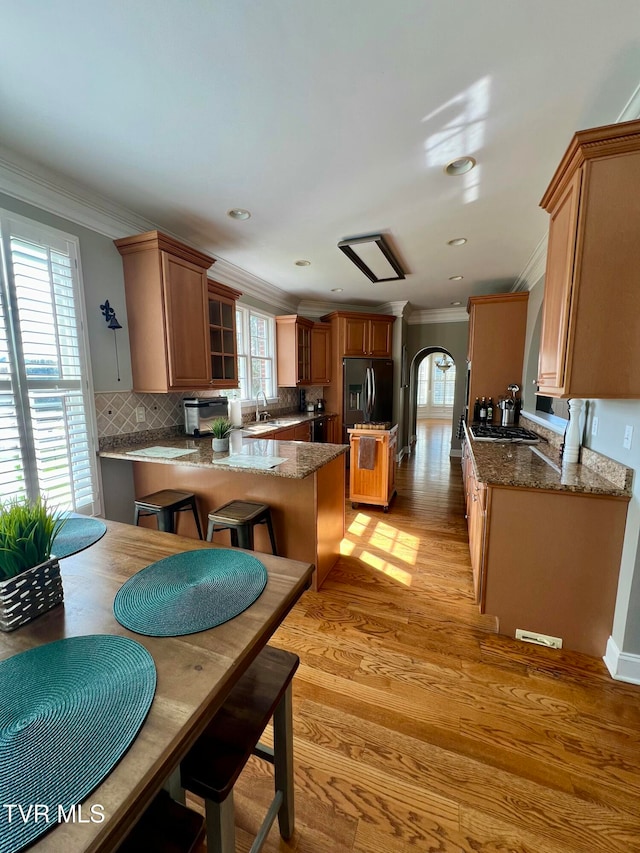 kitchen featuring kitchen peninsula, crown molding, decorative backsplash, light hardwood / wood-style flooring, and refrigerator with ice dispenser