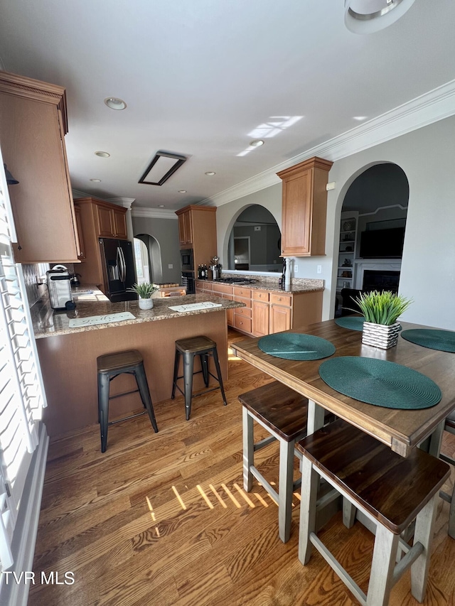 kitchen with black appliances, crown molding, kitchen peninsula, and hardwood / wood-style flooring